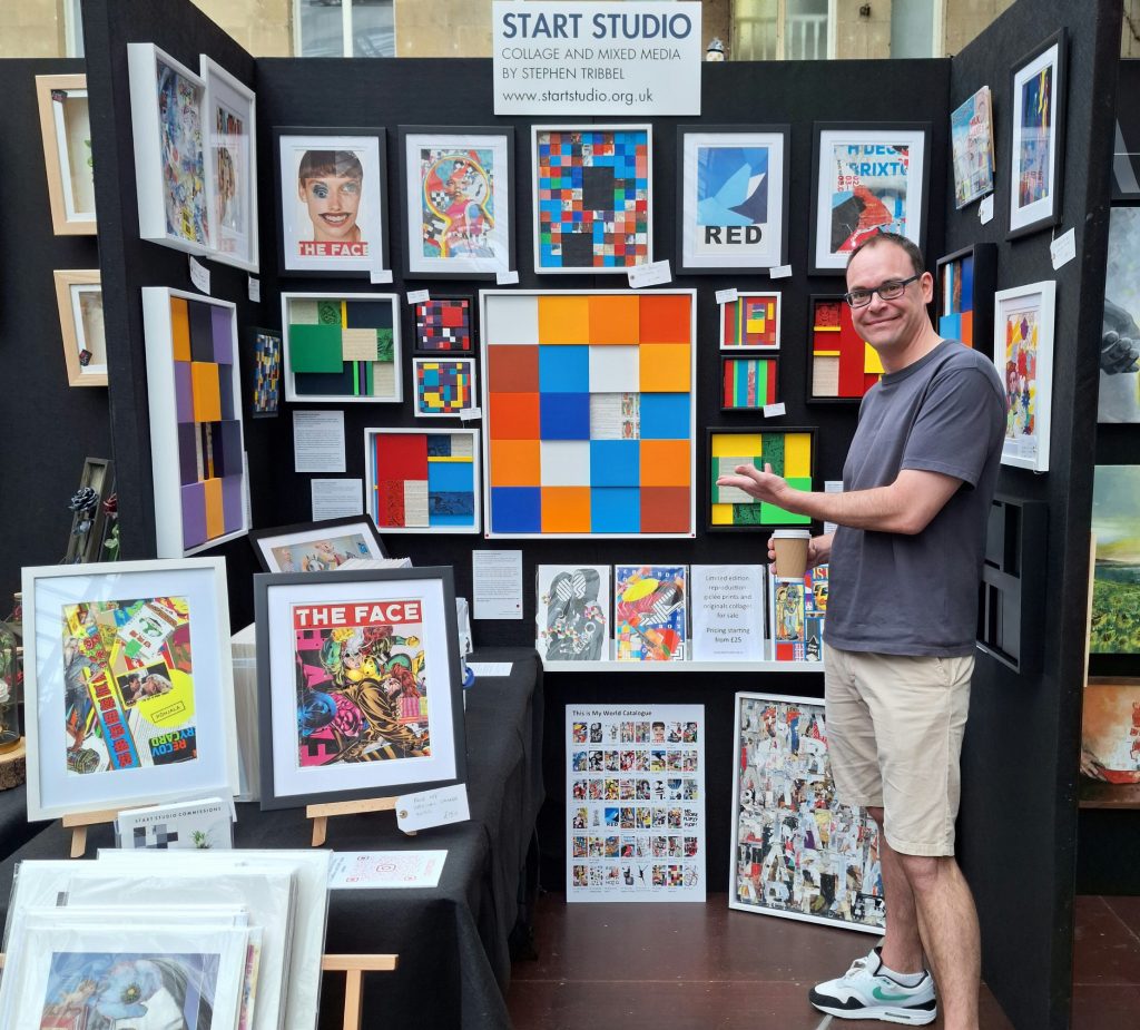Artist Stephen Tribbel in front of Start Studio's stall with original framed artwork hung on black walls at Bath Contemporary Art Fair Sunday 8th September 2024.